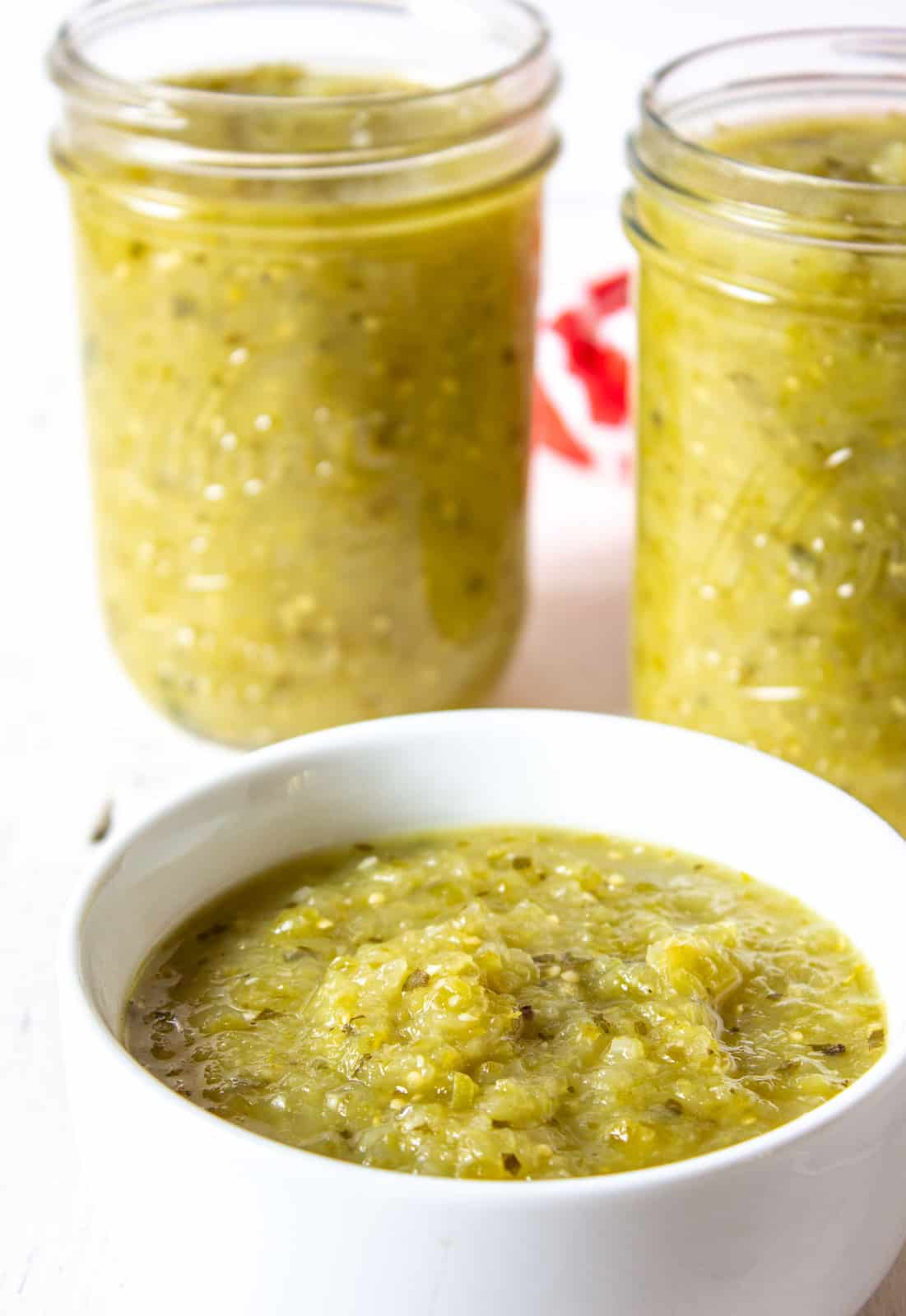 Chunky green sauce in a white bowl and in two glass jars.