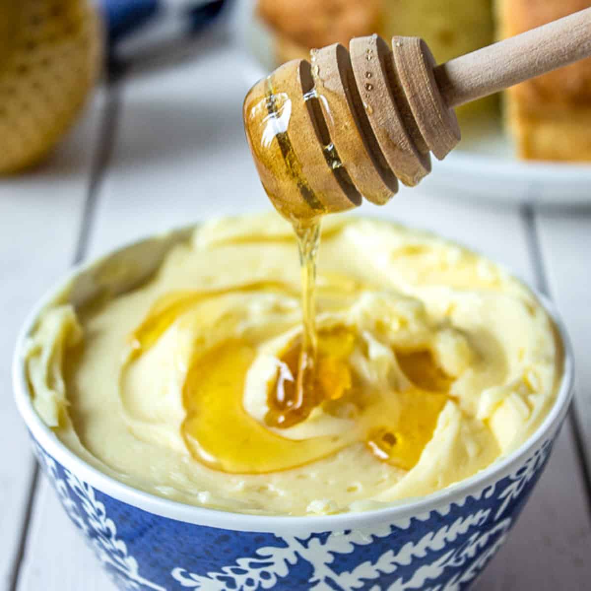 Honey dripping from a wooden dowel onto a bowl of butter.
