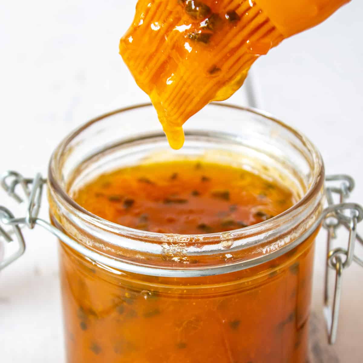 A basting brush dripping with an apricot sauce over a jar filled with the sauce.