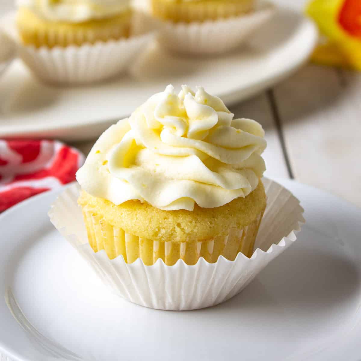 A lemon cupcake topped with a swirl of frosting on a white plate.