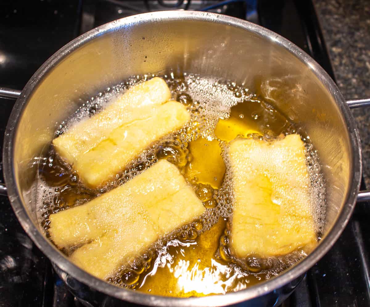 Buttermilk donuts frying in a pot with oil.