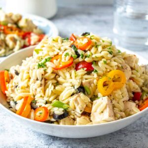 A bowl filled with orzo, bell peppers, tomatoes and chicken.