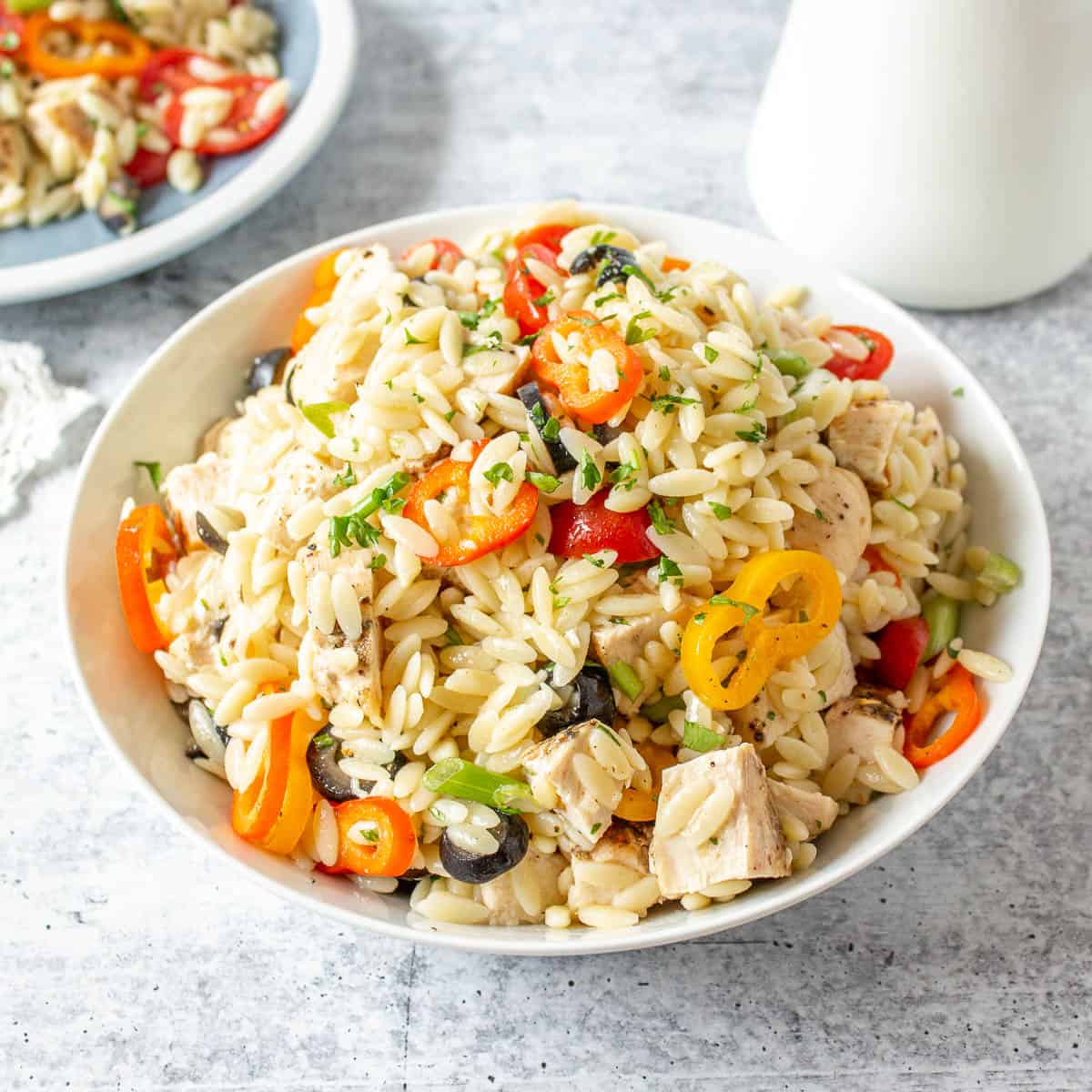 A bowl filled with orzo pasta, sliced tomatoes and chunks of chicken.