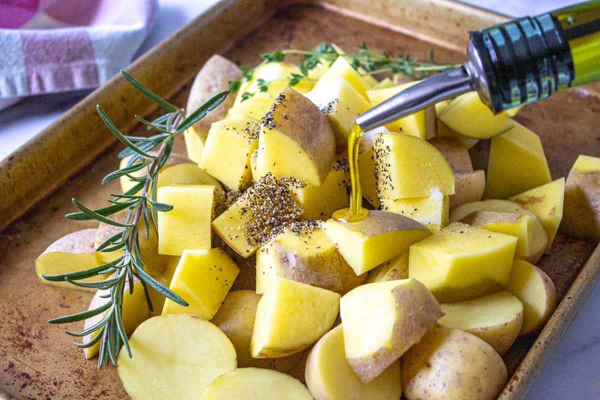 Cut potatoes on a baking sheet with olive oil being drizzled over the potatoes.