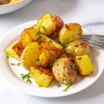 Crispy potato chunks topped with chopped parsley on a white plate.