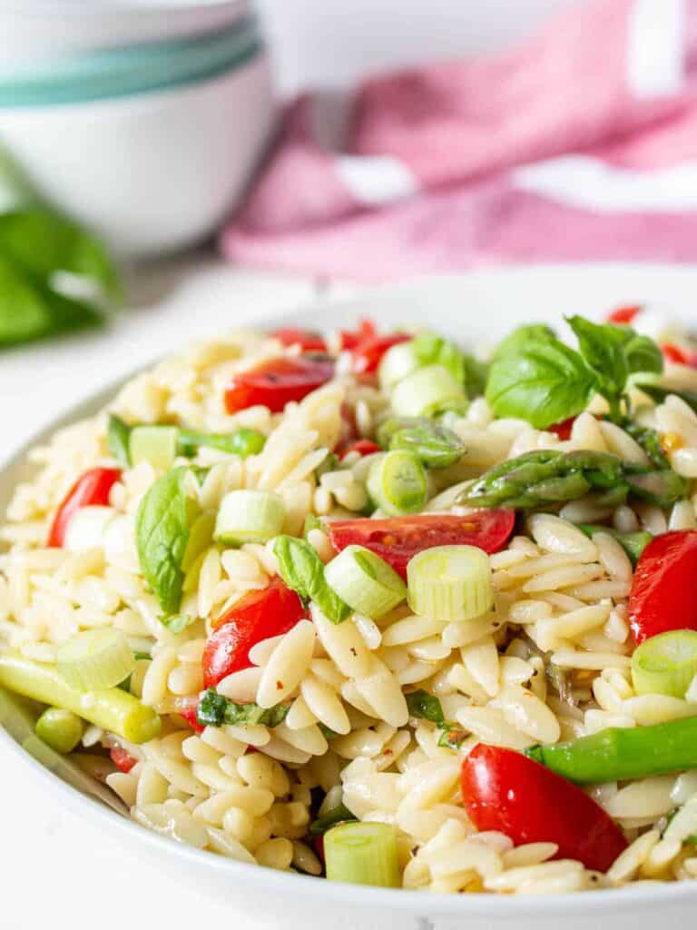 Orzo pasta with chopped asparagus and cherry tomatoes in a white bowl.