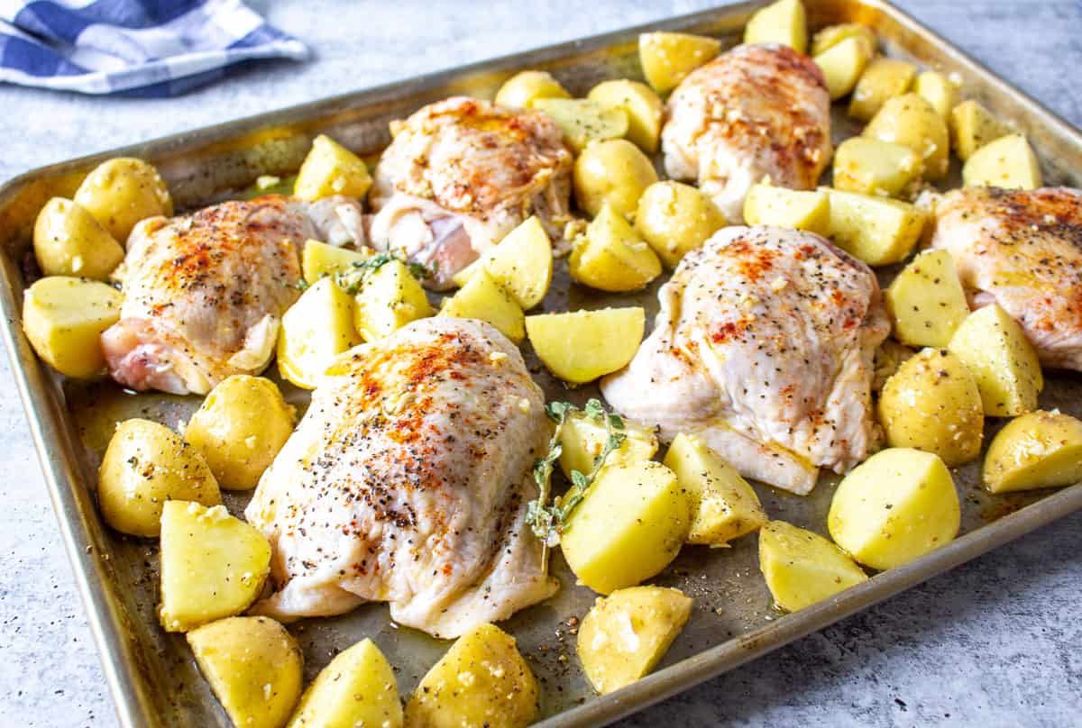 A sheet pan filled with uncooked chicken thighs and cut potatoes.
