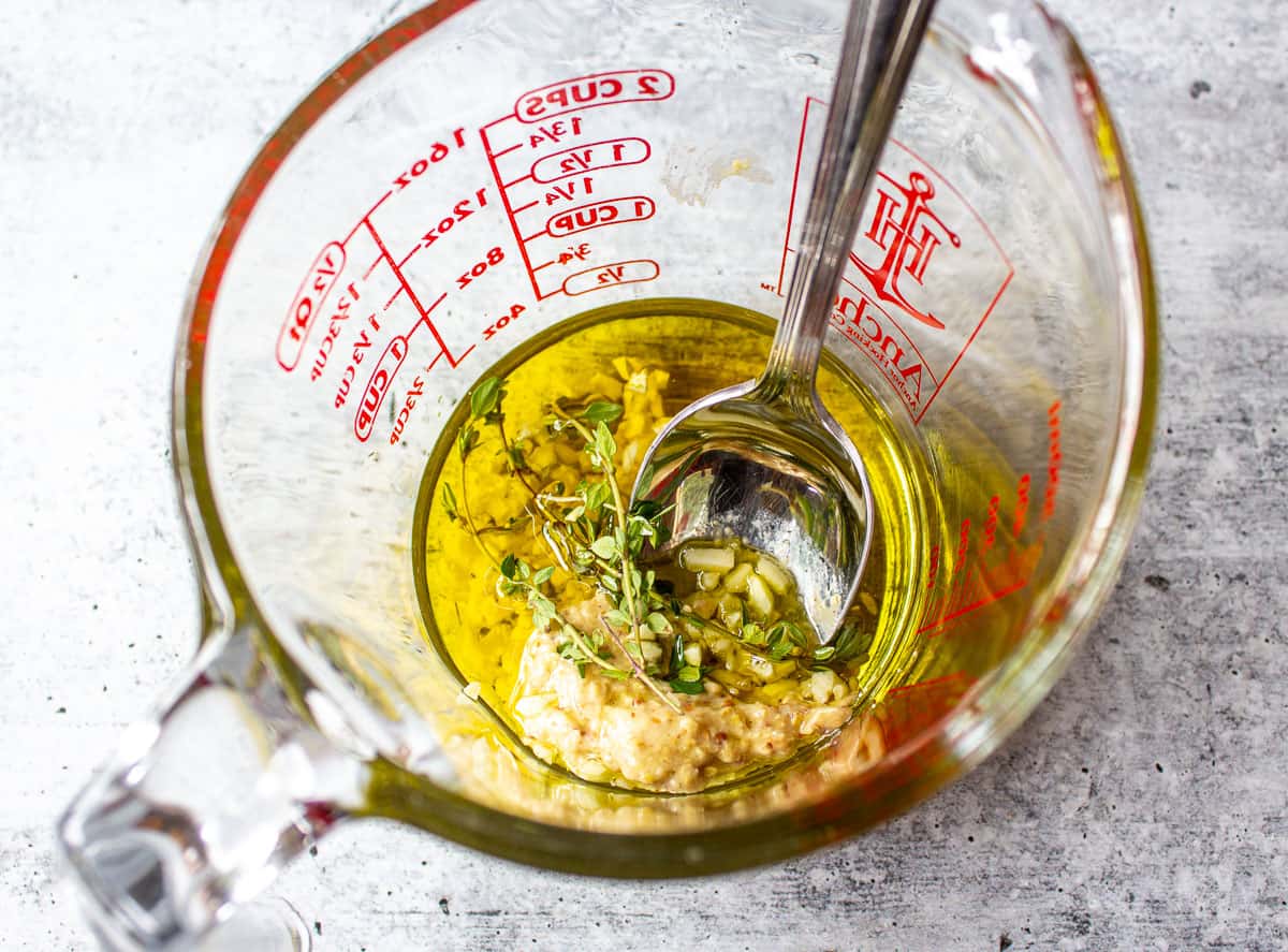 A glass measuring cup filled with olive oil, garlic and fresh thyme.