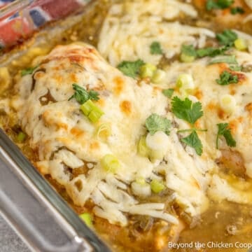 A casserole dish filled with chicken, salsa verde and cheese.