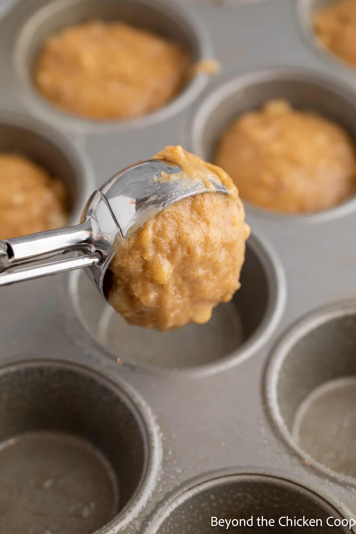 Scooping muffin batter into a muffin tin. 