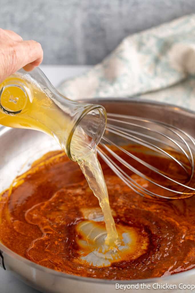 Pouring chicken stock into a pan with seasoning. 