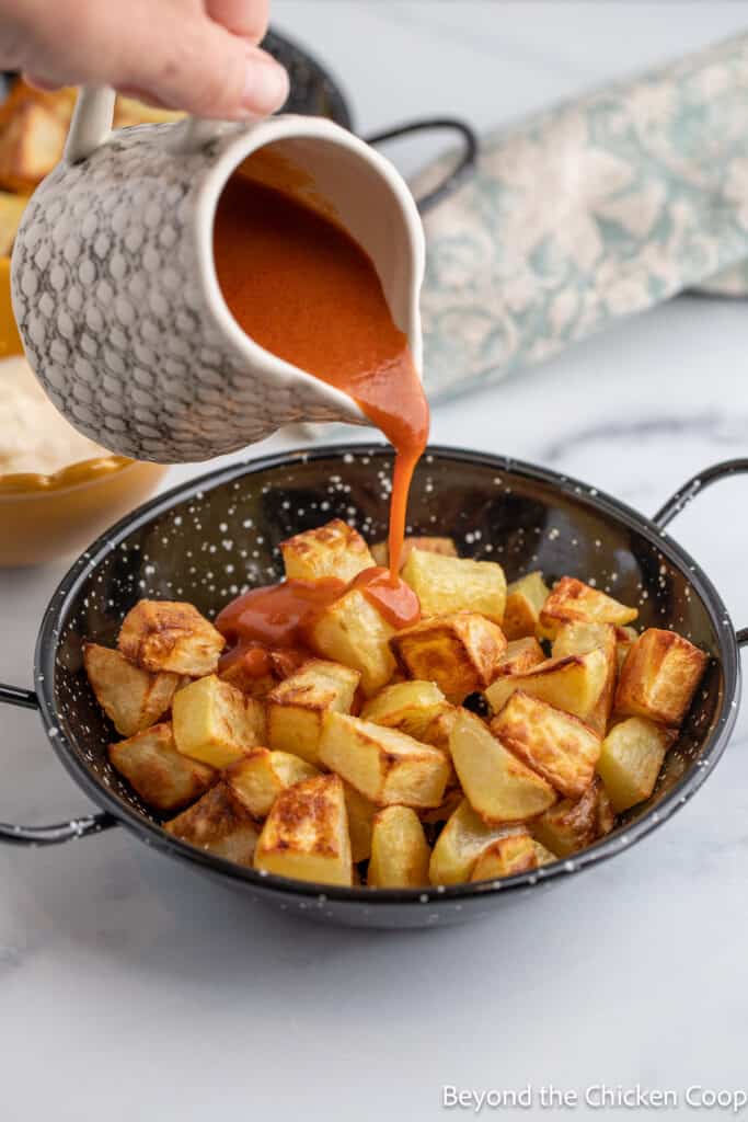 Pouring a red sauce over cooked potatoes. 