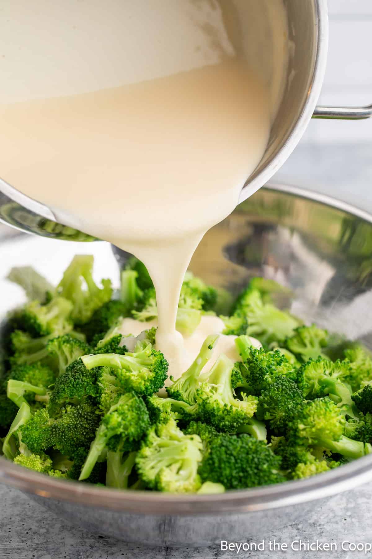 Pouring a creamy sauce over a bowl of broccoli. 