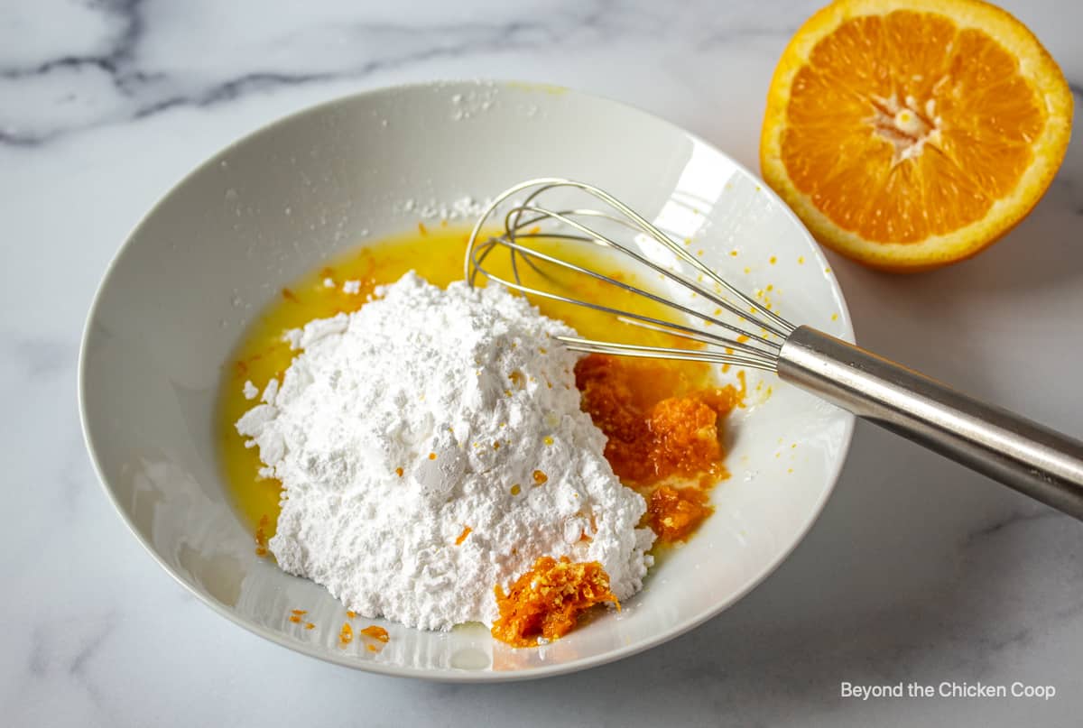 Powdered sugar, orange zest and juice in a bowl with a whisk.