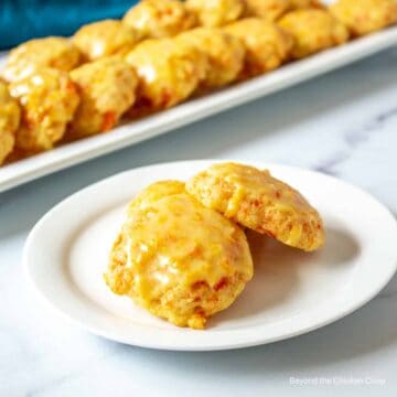 Three cookies with carrots and an orange glaze on a white plate.