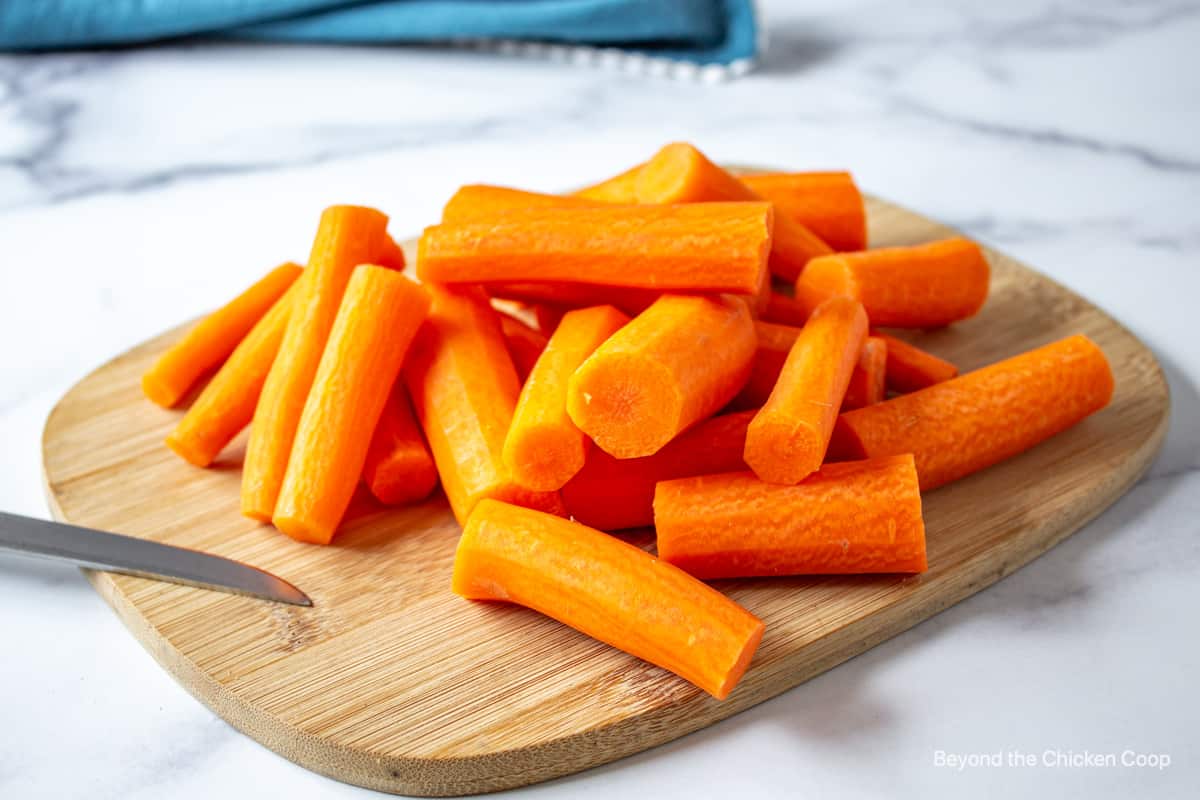 Carrots peeled and cut on a wooden cutting board.