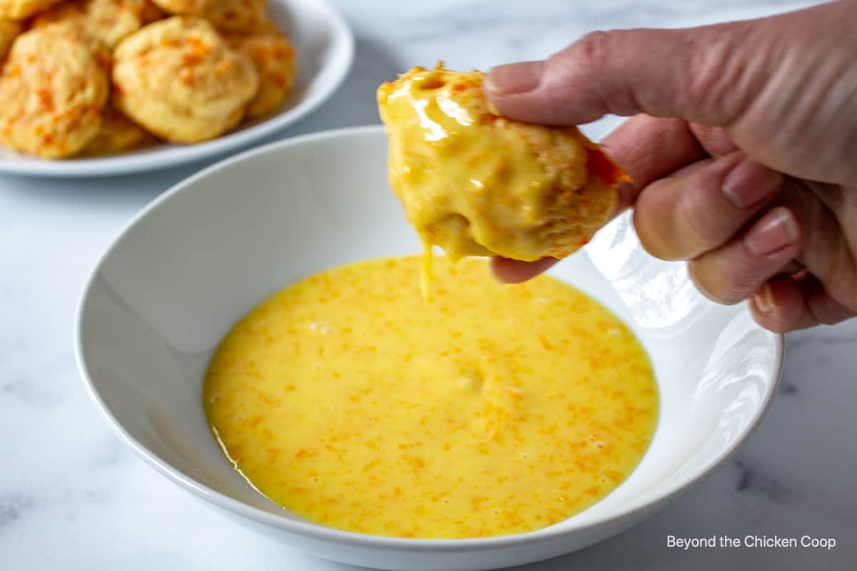 A cookie over a bowl with glaze dripping off the cookie.