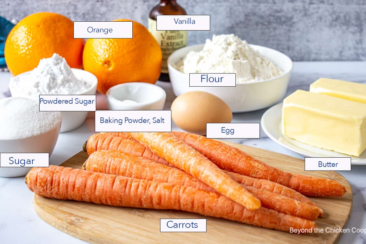 Whole carrots on a cutting board with baking ingredients in the background.