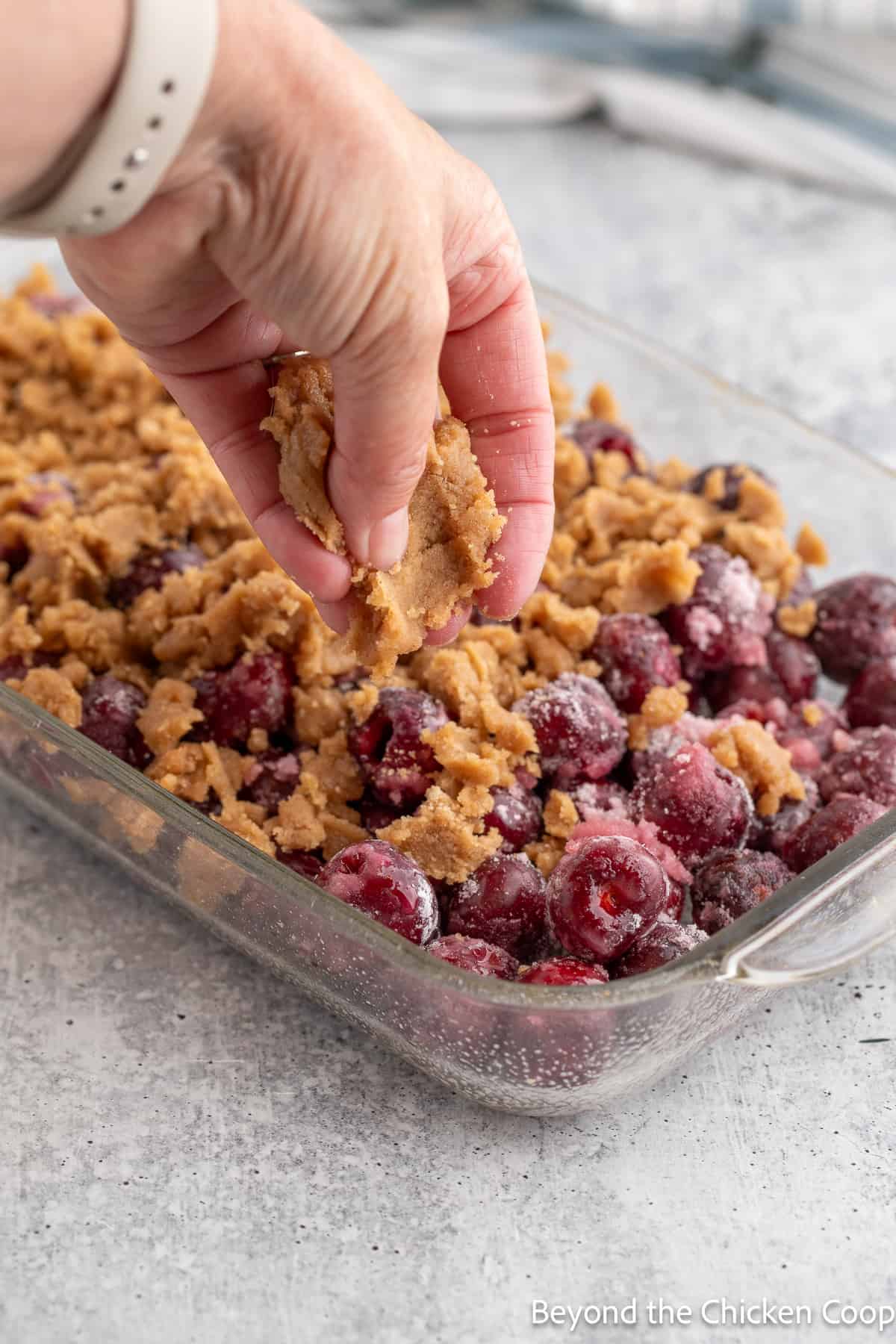 Crumbling a topping onto cherries. 