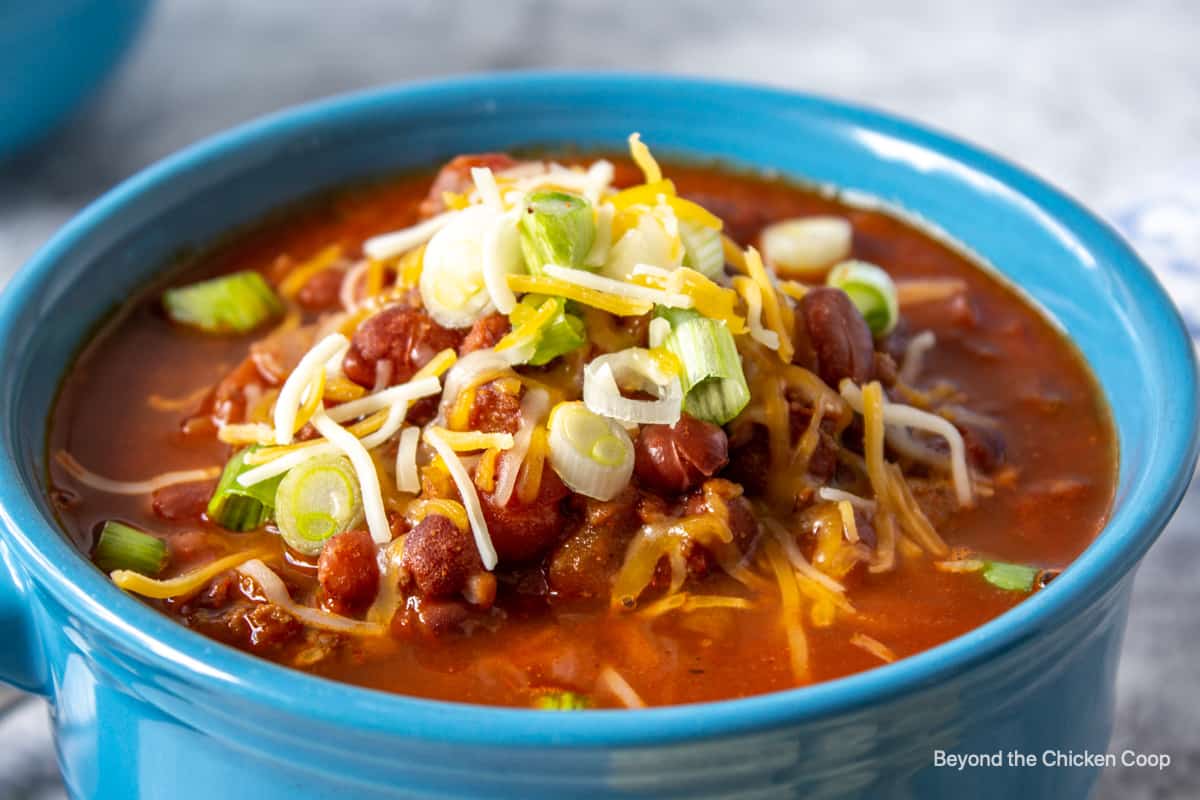 A bowl of chili with beans topped with onions and cheese in a blue bowl.