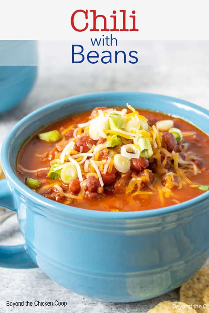 A blue mug filled with chili topped with cheese and onions.