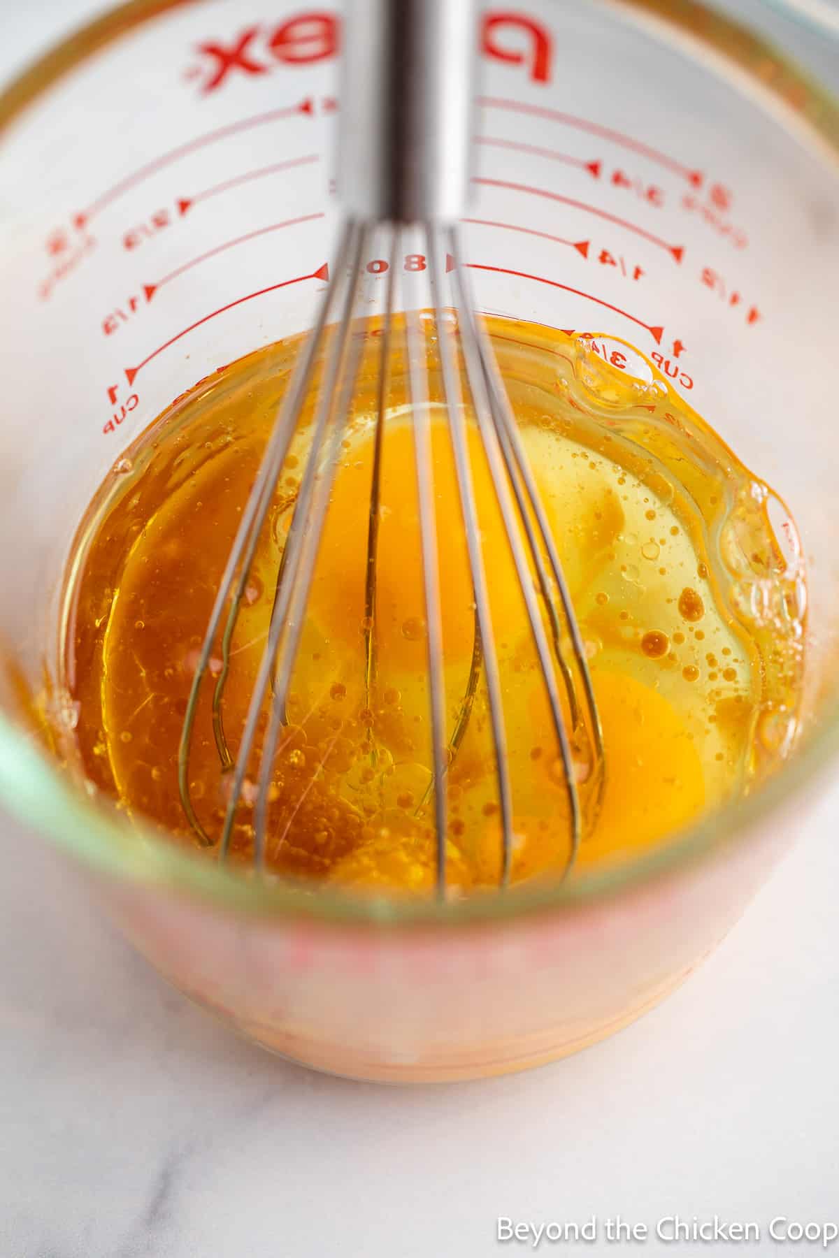 Eggs, oil and vanilla in a measuring cup with a whisk.