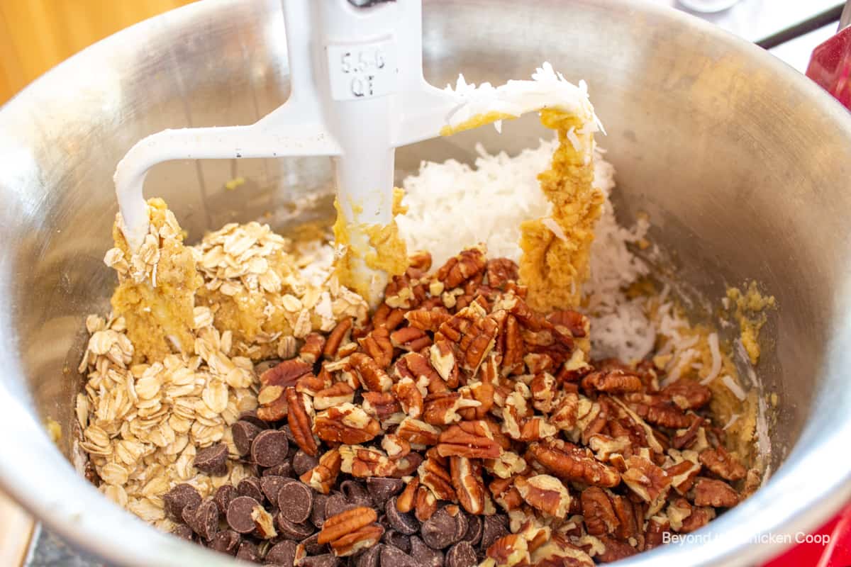 A mixing bowl filled with cookie dough, pecans, chocolate chips, coconut and oats.