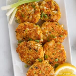 Crispy fish cakes on a white platter with lemon wedges.