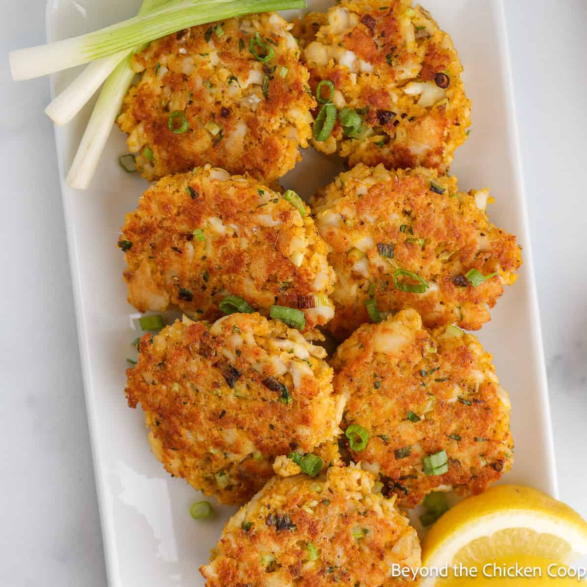 Crispy fish cakes on a white platter with lemon wedges. 