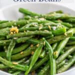 Green beans topped with garlic in a white bowl.