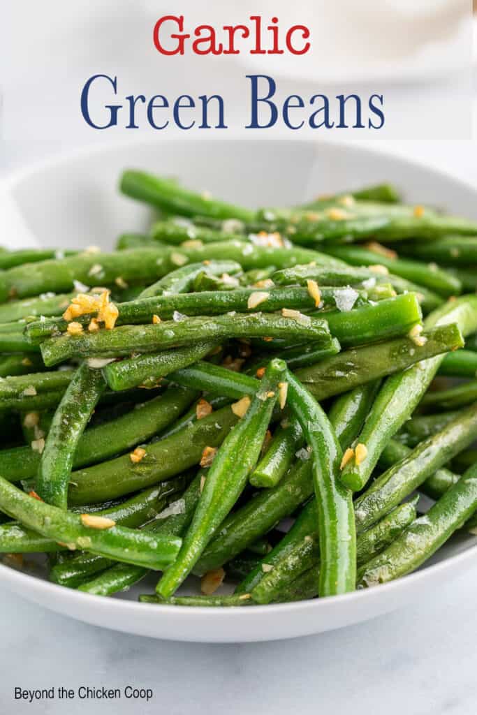 Green beans topped with garlic in a white bowl.