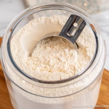 A measuring cup in a glass jar filled with flour.