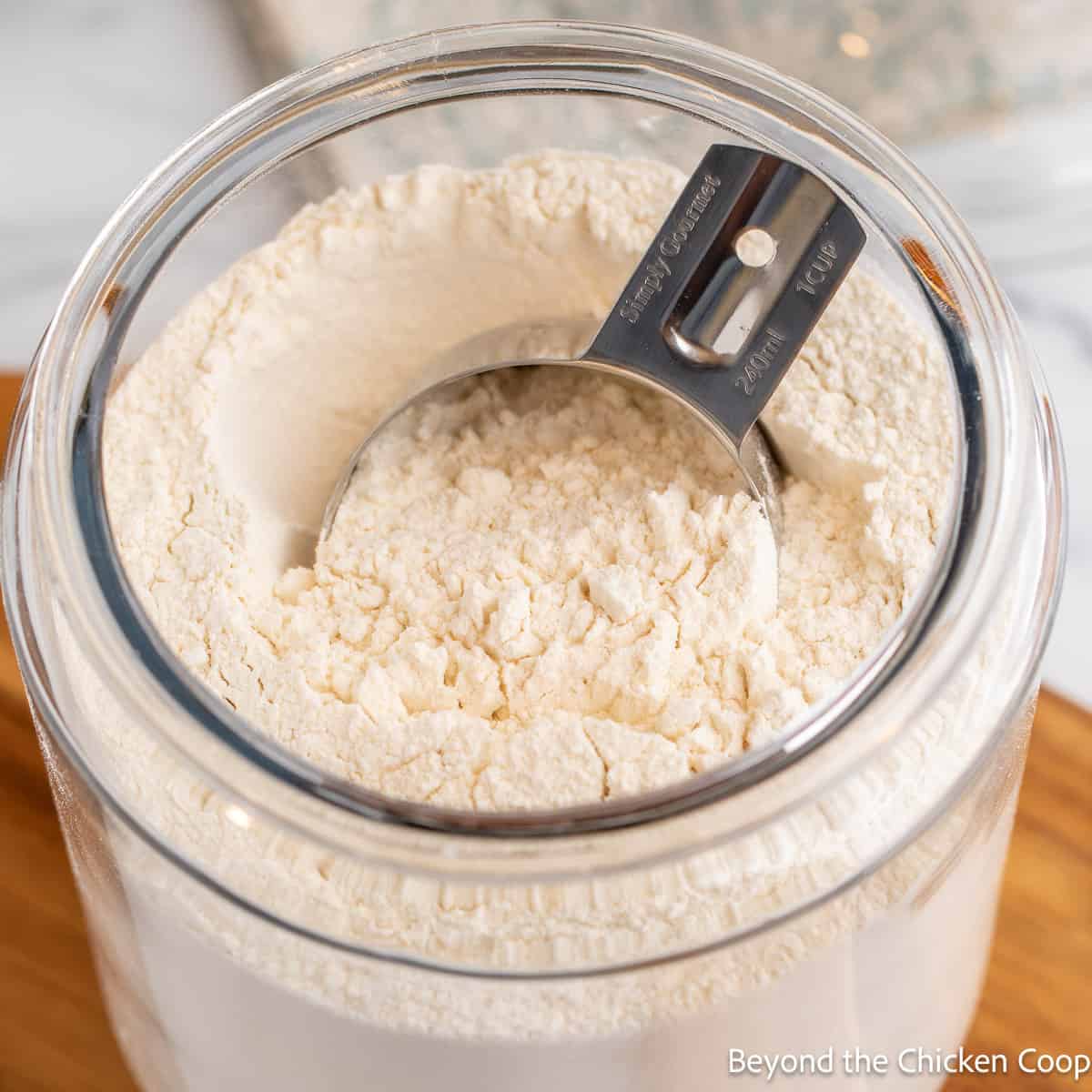 A measuring cup in a glass jar filled with flour. 