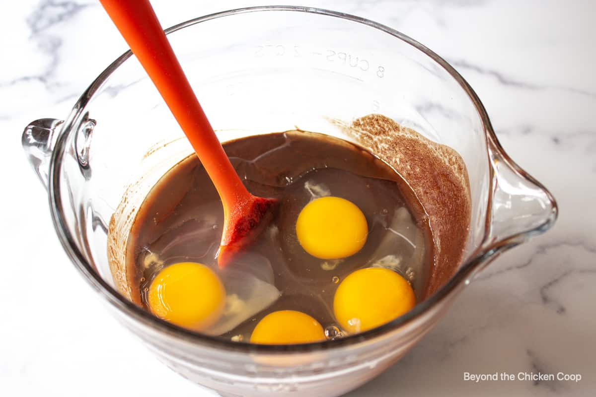 A glass bowl with a chocolate mixture and four eggs.