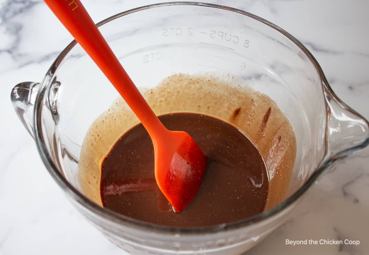 Melted chocoalte in a glass bowl with an orange spatula.