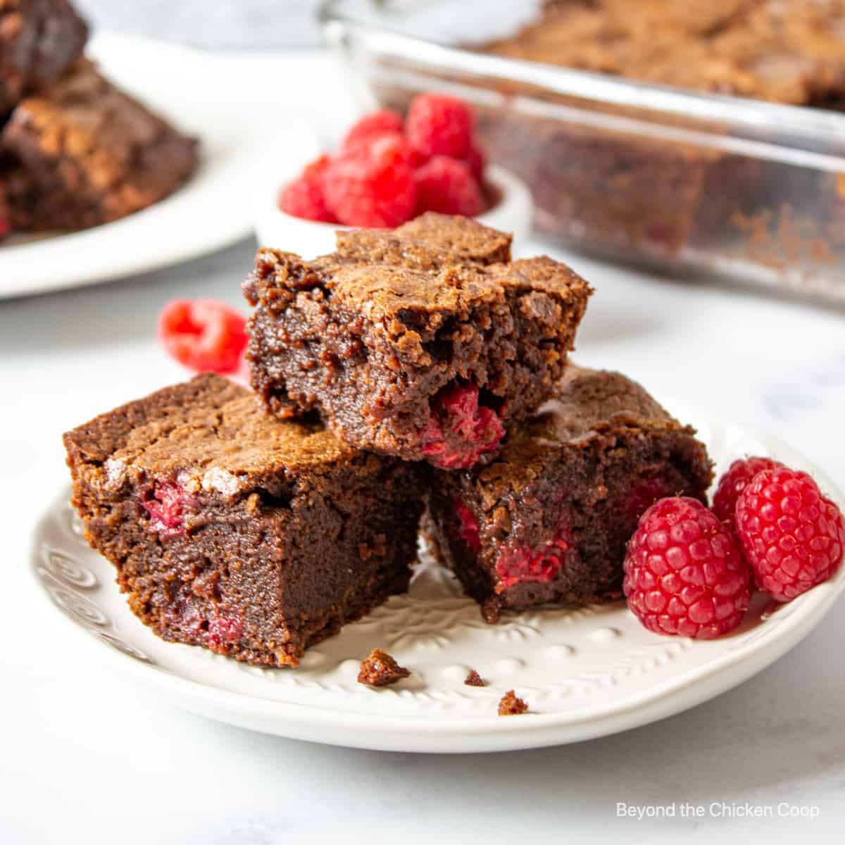 Three raspberry brownies filled with raspberries on a white plate.