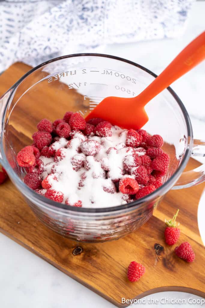 Combining raspberries and sugar together in a bowl. 