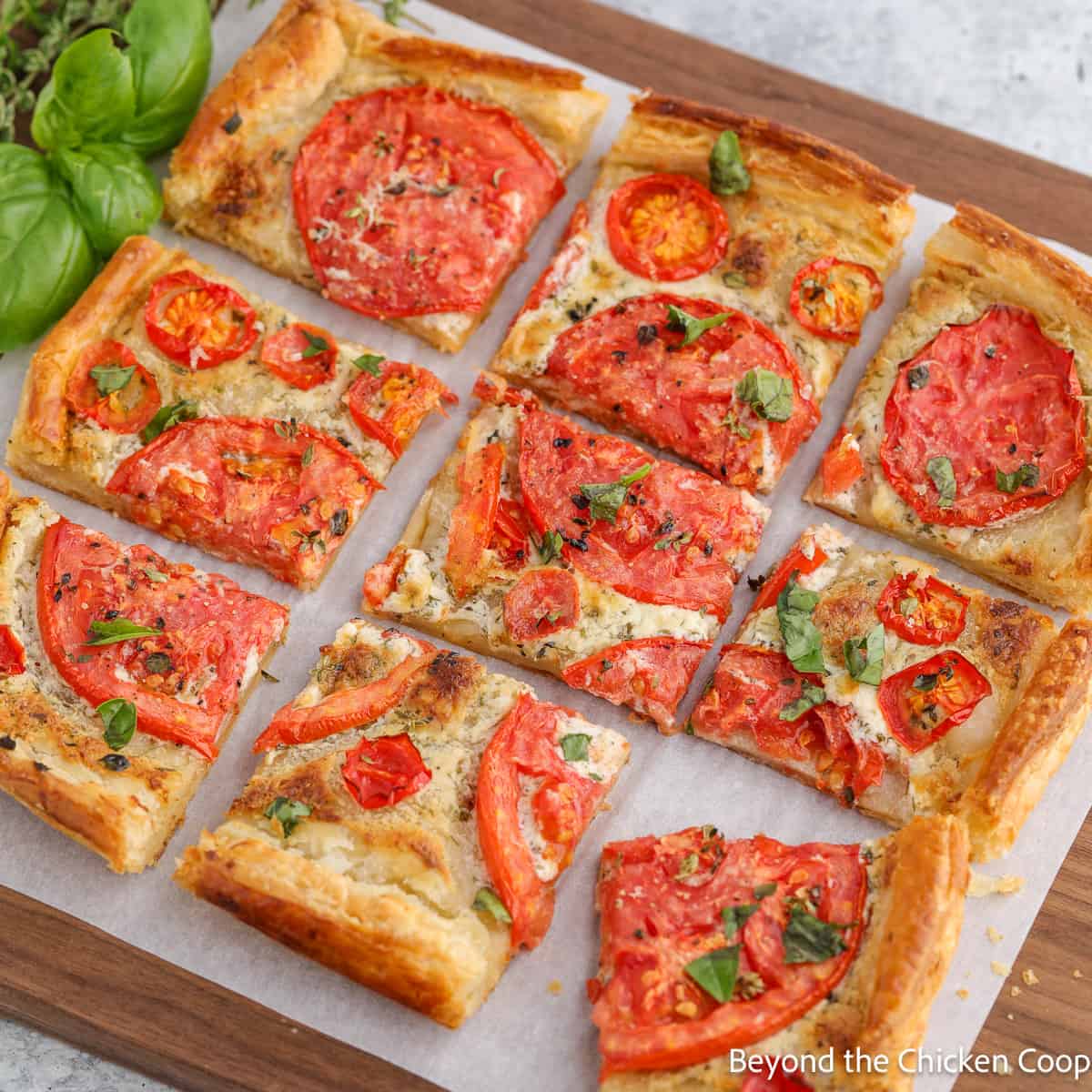 A tomato tart cut into nine pieces on a wooden board.