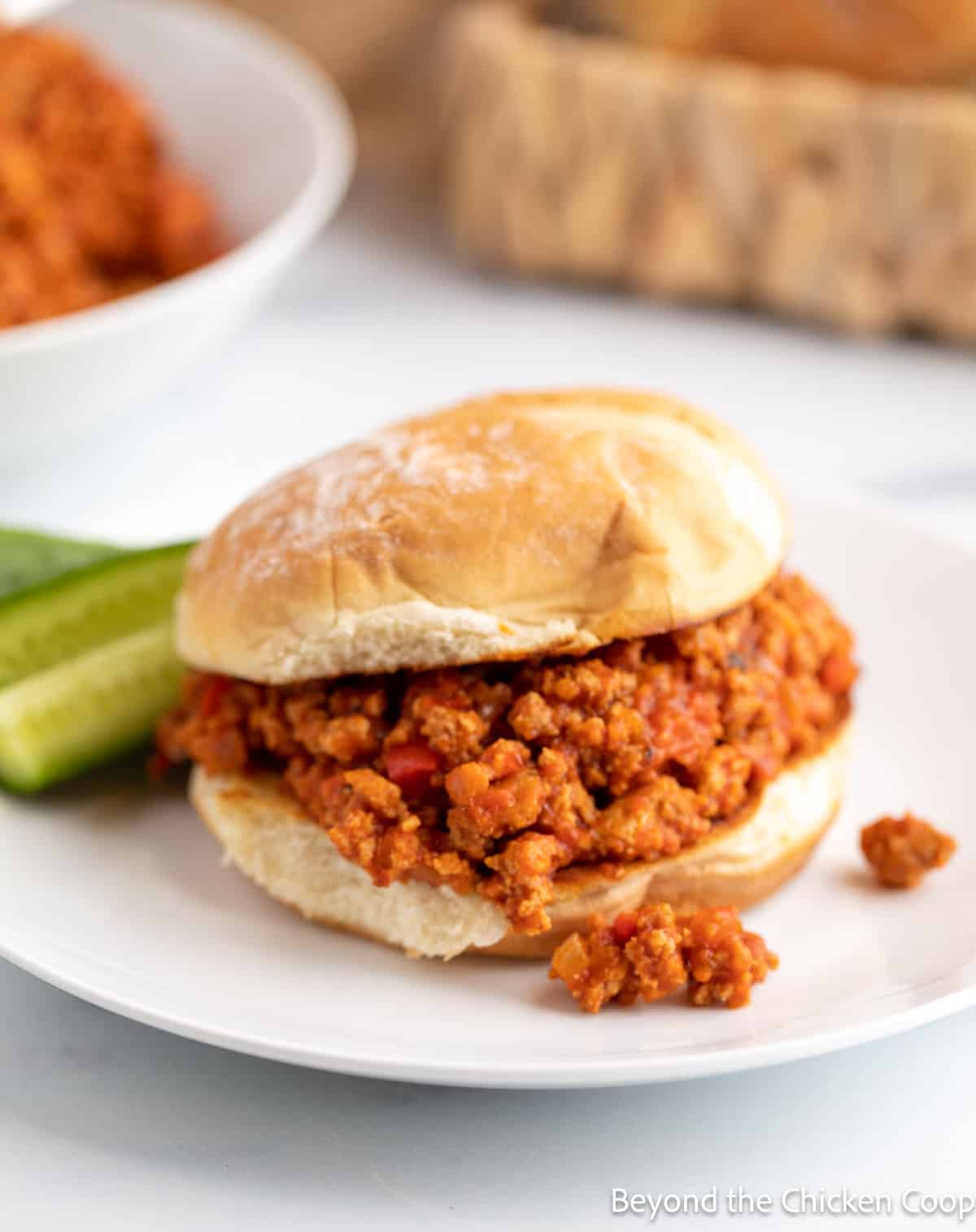 Sloppy Joe sandwich on a plate with cucumber spears. 