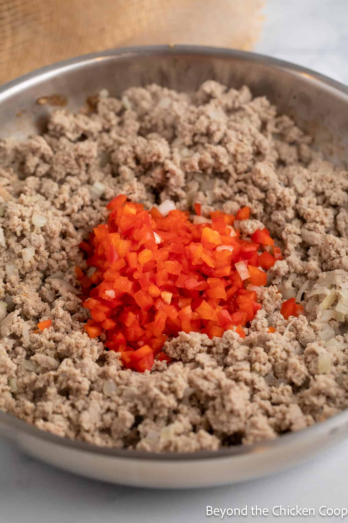 Chopped bell pepper in a pan with browned burger. 