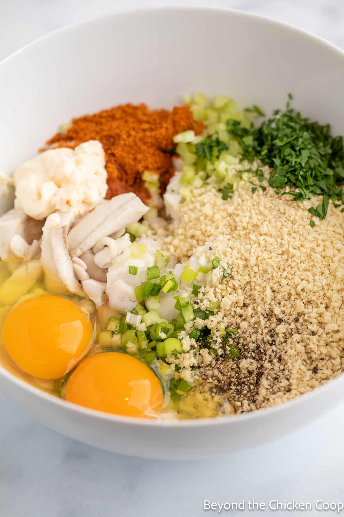 A bowl filled with white fish, eggs, bread crumbs and seasoning.