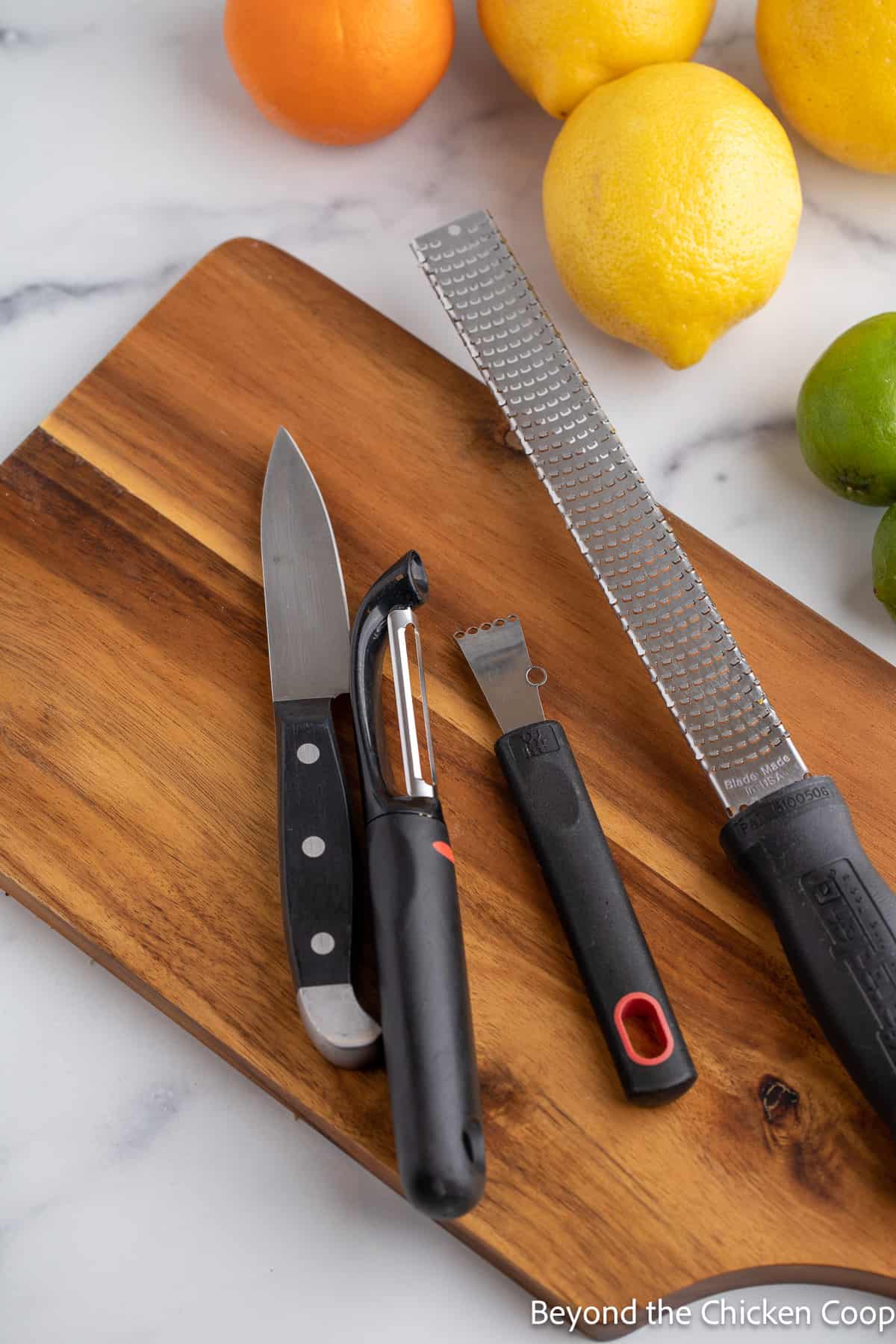 A small knife, a peeler, a zester and a grater on a wooden board. 