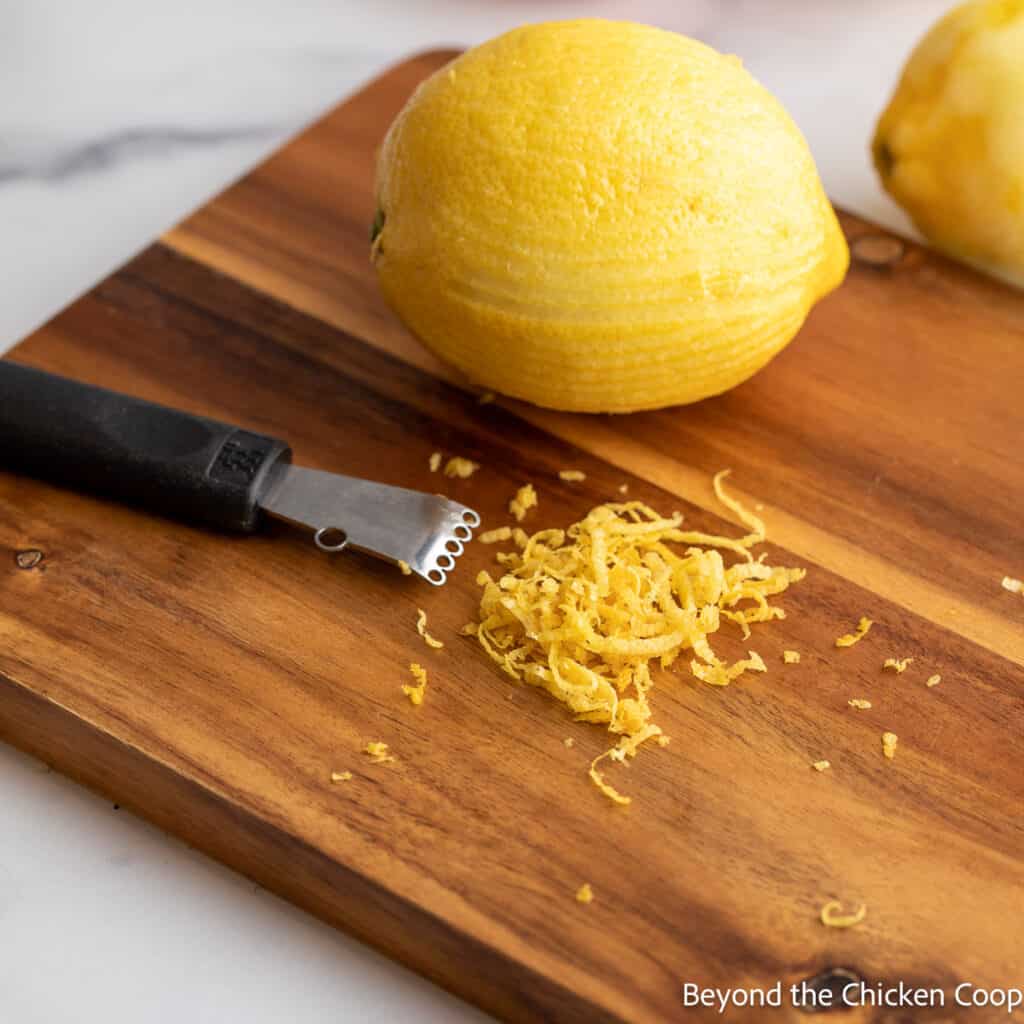 A citrus zester tool next to a lemon and a pile of zest. 