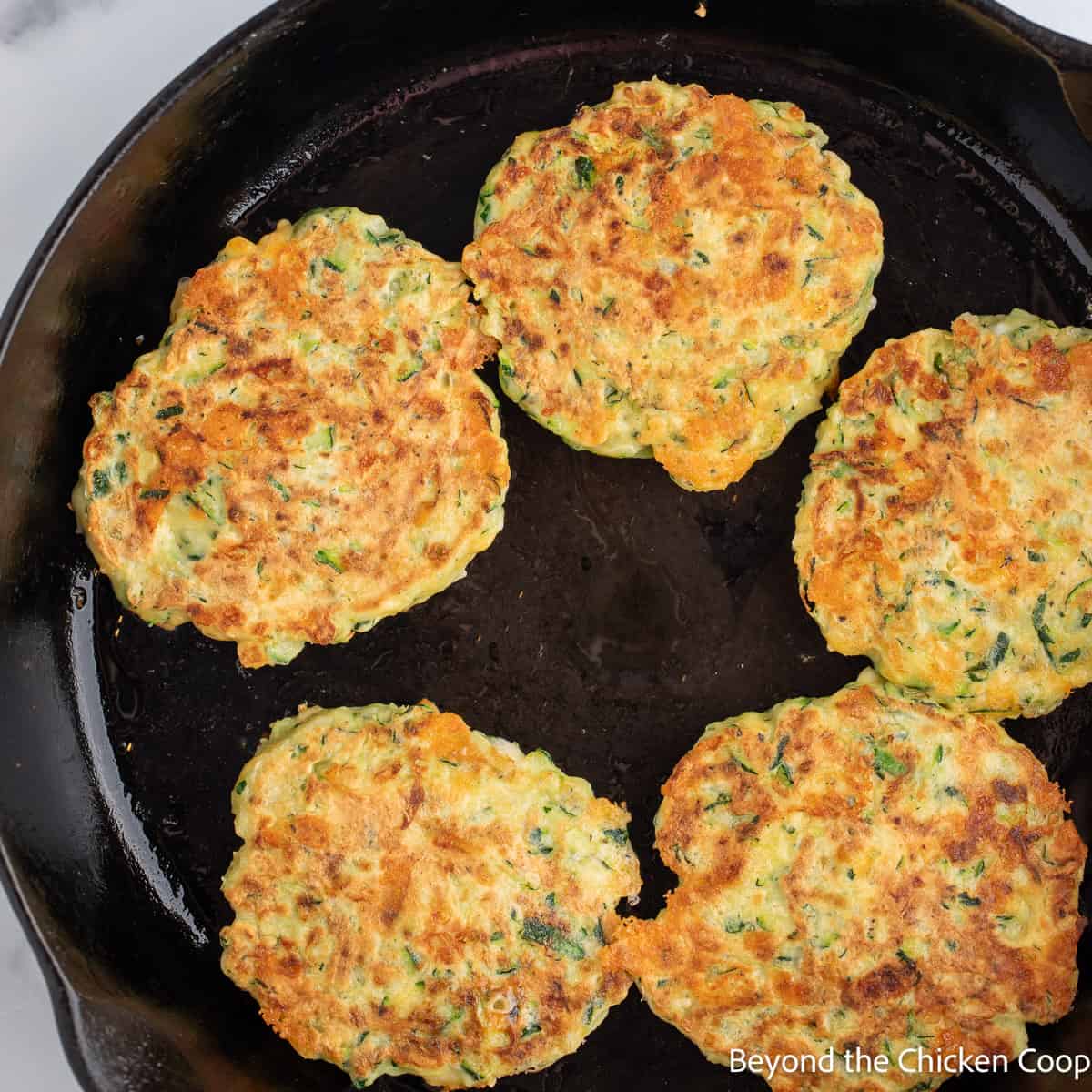 Cooked zucchini fritters in a skillet. 