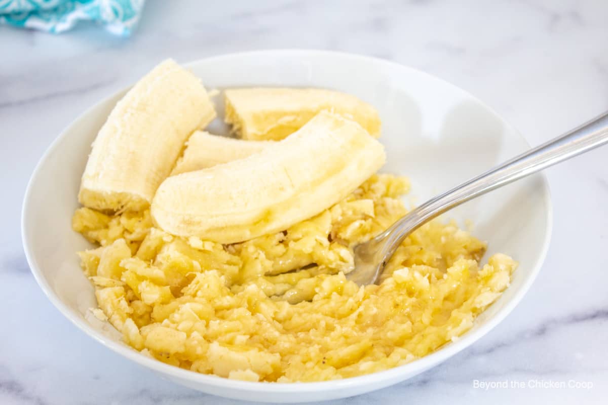 Mashed bananas with a fork in a white bowl.