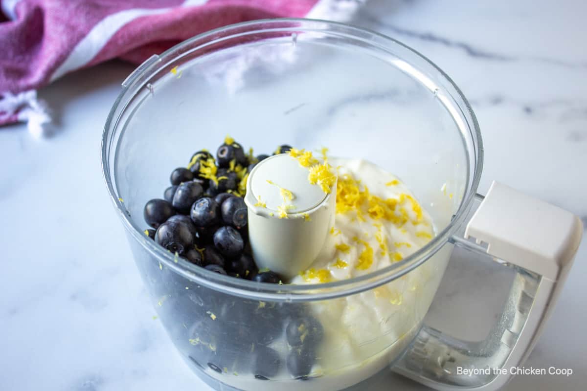 Blueberries with lemon zest in a food processor bowl.