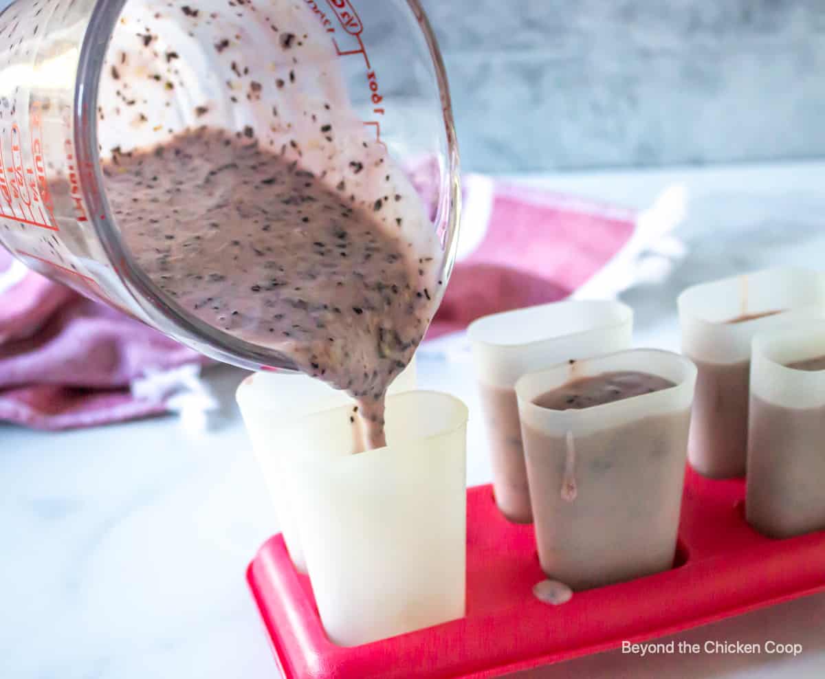 A blueberry mixture being poured into popsicle cups.