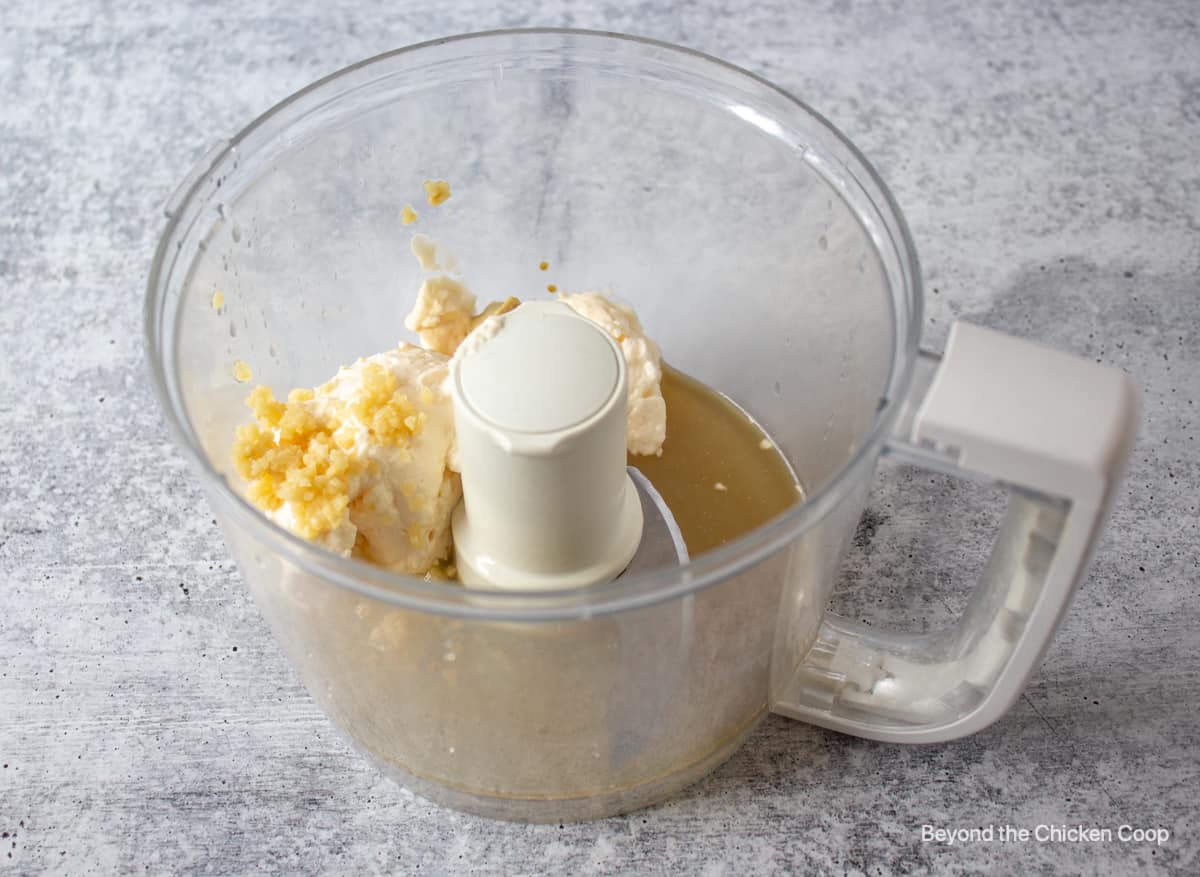 A food processor bowl with mayonnaise, garlic and lemon juice.