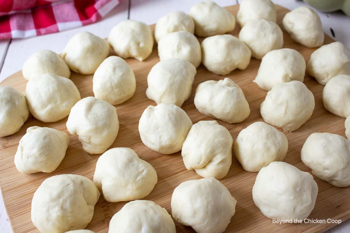 Round balls of bread dough on a wooden cutting board.