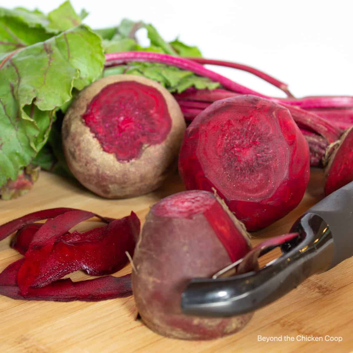 Fresh beets being peeled with a vegetable peeler.